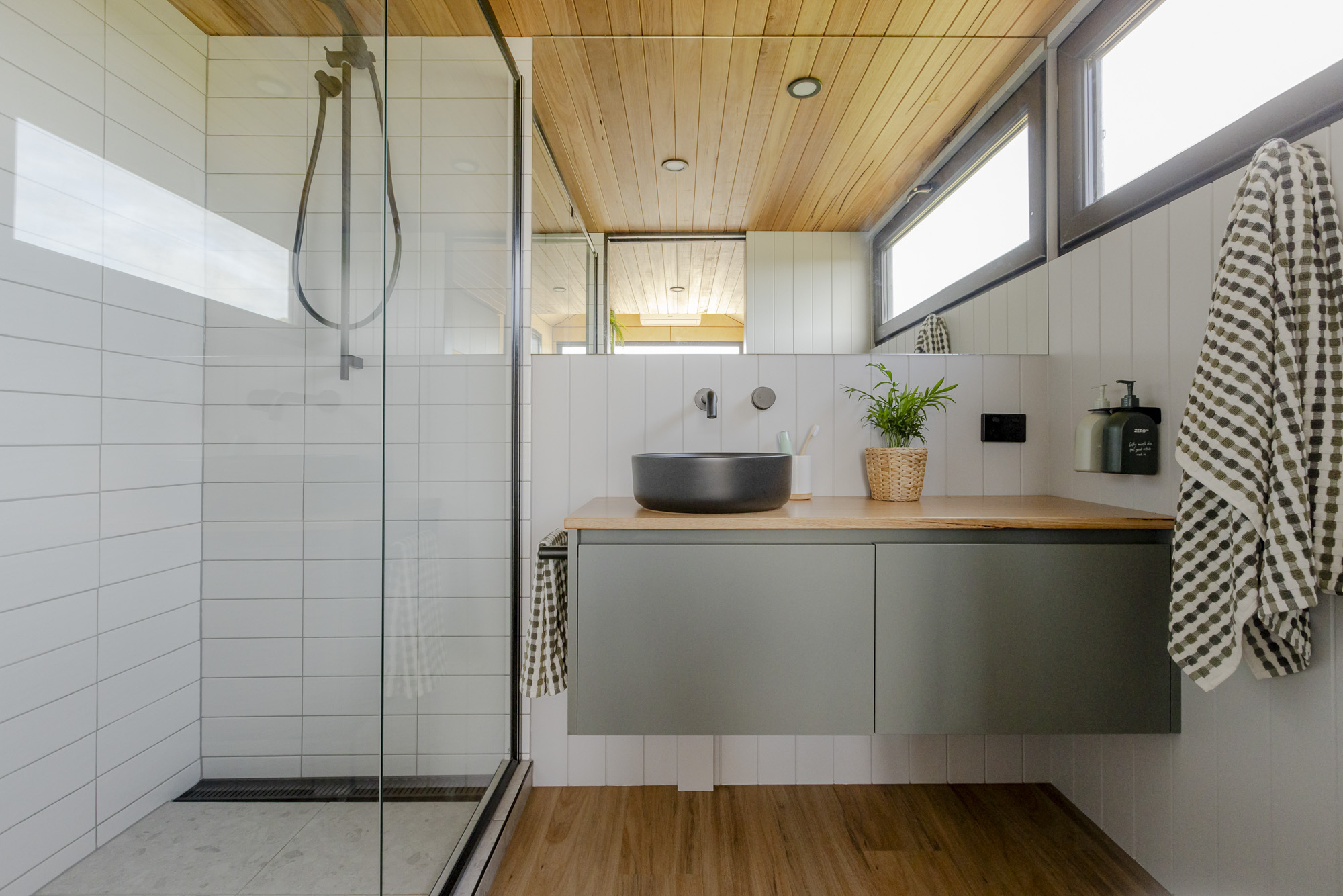 Bathroom with tiled walls, floating timber vanity and matte black basin in a tiny home on wheels