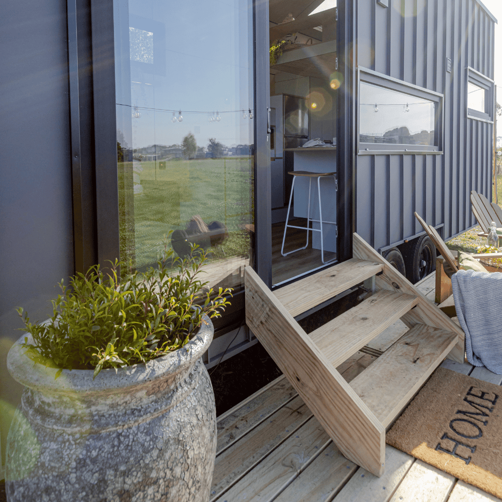 Set of sturdy treated pine steps leading to a tiny home entrance with a cozy outdoor seating area and a welcoming doormat