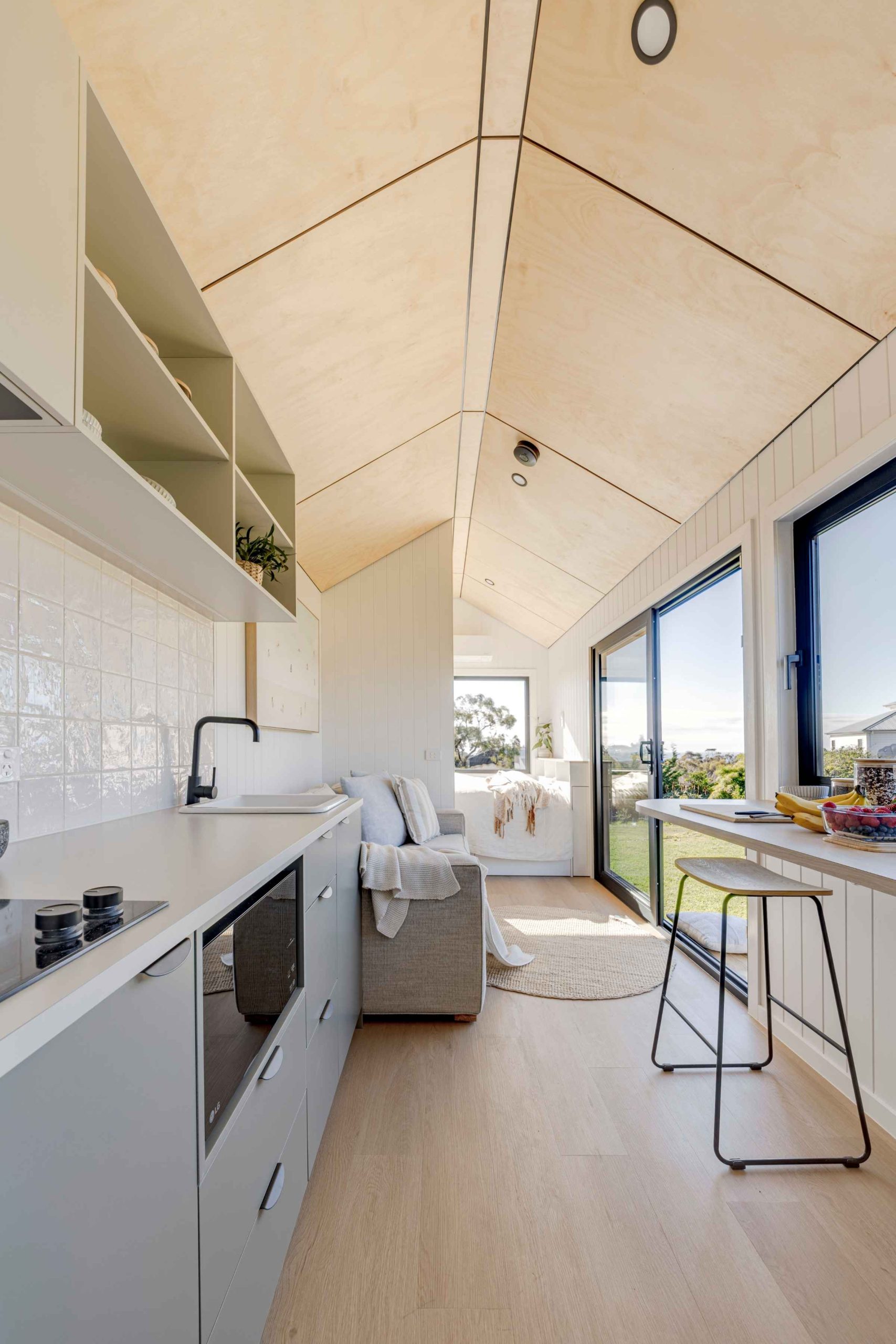 Sunrise Haven tiny home on wheels interior showing the kitchen, breakfast bar, sofa and ground-floor bedroom beneath a timber ceiling.